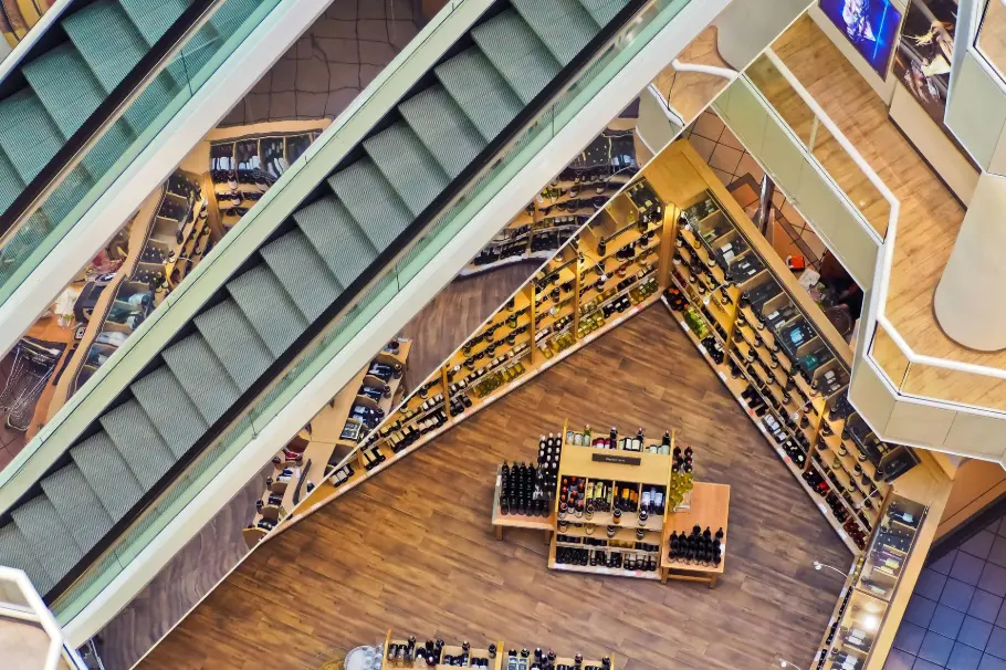 Vue de dessus d'un magasin moderne avec un sol en bois, des escalators et des étagères de produits bien organisées. Représente comment le parfum améliore l'expérience d'achat en créant une atmosphère accueillante et mémorable grâce à la diffusion d'huiles essentielles.